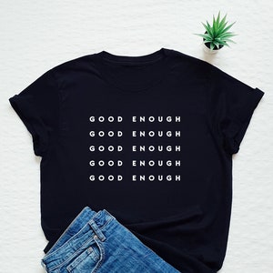 May include: Black t-shirt with the phrase "GOOD ENOUGH" repeated five times in white text.