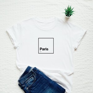 May include: White t-shirt with a black square and the word "Paris" inside.