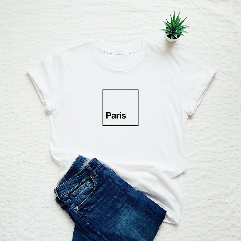 May include: White t-shirt with a black square and the word "Paris" inside.