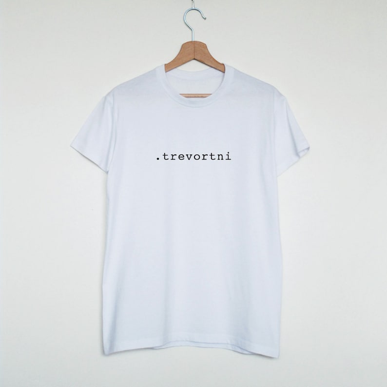 Op de afbeelding: Wit T-shirt met de tekst ".trevortni" in zwart gedrukt op de voorkant.