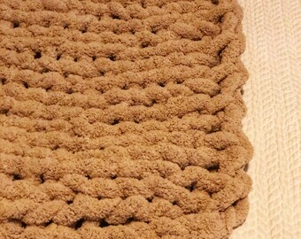 May include: A close-up of a brown chunky knit blanket with a soft, fuzzy texture. The blanket is made with thick yarn and has a simple, woven pattern.