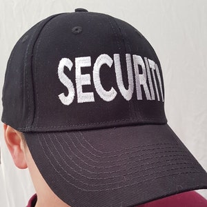May include: A black baseball cap with a white embroidered "SECURITY" text on the front.