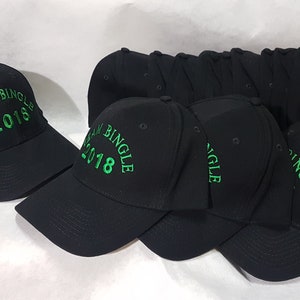 Puede incluir: Un grupo de gorras de béisbol negras con bordados verdes. Las gorras dicen "Team Bingle 2018".