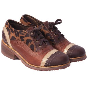 K&ouml;nnte beinhalten: Braune Lederschn&uuml;rschuhe mit Leopardenmuster und goldenen Akzenten. Die Schuhe haben einen dicken Absatz und eine runde Spitze.