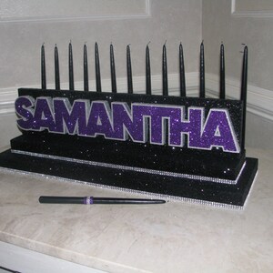 May include: A black and purple candle holder with the name Samantha spelled out in glitter. The holder has 18 black candles and is decorated with rhinestones.