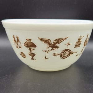 Peut inclure: Bol en céramique blanc avec un motif brun représentant divers objets, dont un aigle, une lampe, un moulin à café et un soufflet.