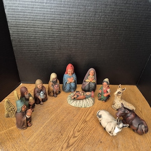 Könnte beinhalten: Eine Keramik-Weihnachtskrippe mit Figuren von Maria, Josef, dem Jesuskind, den drei Weisen, einem Engel und verschiedenen Tieren. Die Figuren sind in gedämpften Braun-, Blau-, Rot- und Grüntönen bemalt und schaffen eine traditionelle Urlaubsszene.