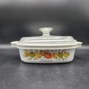 Puede incluir: Plato de cerámica blanca para hornear con tapa de vidrio. El plato tiene un diseño floral con verduras y champiñones. El texto "L'Echalote" está impreso en el plato.