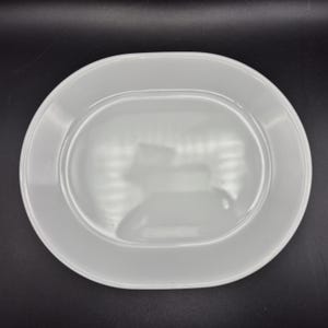 May include: A white oval serving platter with a slightly raised rim. The plate has a smooth, glossy finish and is set against a dark background. This dish is suitable for serving appetizers, entrees, or desserts.