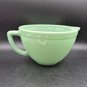 Puede incluir: Un cuenco para mezclar de color verde claro con asa y boquilla. El cuenco es de vidrio y tiene un acabado liso y brillante. El cuenco está diseñado para mezclar ingredientes en la cocina.