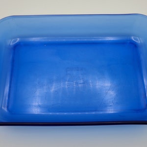 Könnte beinhalten: Eine rechteckige Auflaufform aus kobaltblauem Glas mit abgerundeten Ecken und zwei seitlichen Griffen. Die Form ist leer und scheint aus einem einzigen Glasstück zu bestehen. Die Form ist etwa 30 cm lang und 20 cm breit.