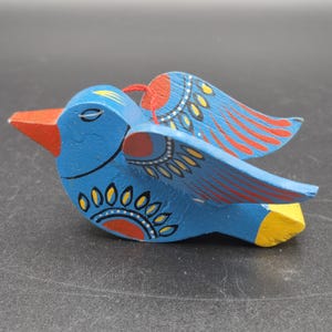 May include: A hand-painted wooden bird figurine in shades of blue, red, yellow, and white. The bird has detailed wings and a red beak. The figurine is a decorative item.