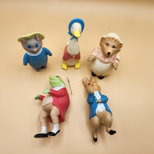 Könnte beinhalten: Fünf kleine, bunte Figuren von Charakteren aus dem Kinderbuch 'Die Geschichte vom Peter Hase'. Die Figuren sind Peter Hase, ein Frosch, ein Igel, eine Ente und eine Katze. Die Figuren sind aus Plastik und etwa 7,5 cm groß.