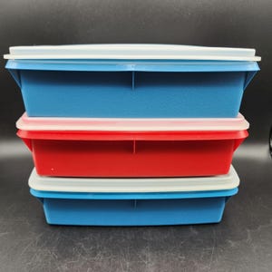 Könnte beinhalten: Drei Plastik-Aufbewahrungsbehälter, die übereinander gestapelt sind. Der obere Behälter ist blau mit einem weißen Deckel. Der mittlere Behälter ist rot mit einem weißen Deckel. Der untere Behälter ist blau mit einem weißen Deckel.