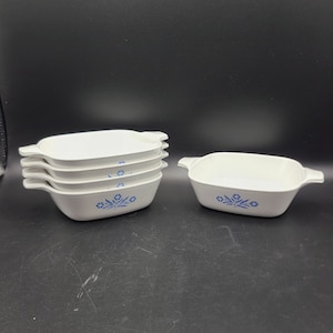 Könnte beinhalten: Ein Set aus sechs weißen, rechteckigen Backformen mit Griffen. Jede Form hat ein blaues Blumendesign auf der Vorderseite. Die Formen sind gestapelt und auf einer dunklen Oberfläche angeordnet, was ihr klassisches Design zeigt.