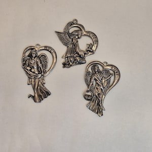 Può includere: Tre ornamenti a forma di angelo color argento. Ogni angelo è all'interno di una cornice a forma di cuore. Un angelo tiene delle stelle, un altro una colomba e il terzo un cestino. Le parole "HOPE", "PEACE" e "LOVE" sono incise sui telai.