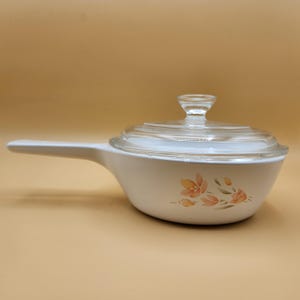 Puede incluir: Sartén de cerámica blanca con tapa de vidrio y diseño floral. Las flores son de color naranja y marrón.