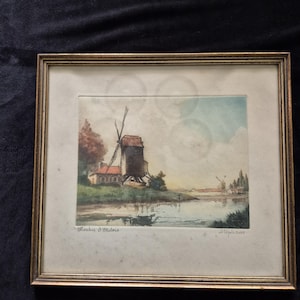 May include: A framed watercolour painting depicting a windmill by a river, titled Moulin d'Outois and signed Stephans. The artwork features a rustic building with a red roof, green landscape, and a pale blue sky, enclosed in a gold-toned frame.