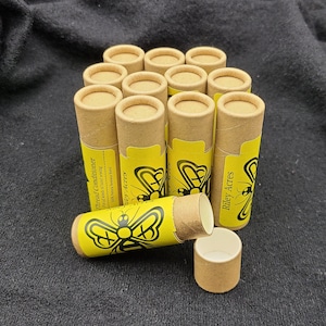 May include: A group of 10 brown cardboard tubes with yellow labels. The labels feature a black bee illustration and the text "Riley Acres". One tube is open, revealing a white interior.
