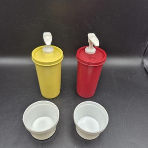 Pode incluir: Dois dispensadores de condimentos, um amarelo e outro vermelho, com tampas de bomba brancas. Dois recipientes brancos com fundo redondo também estão na imagem. Os dispensadores são provavelmente para condimentos como ketchup e mostarda.