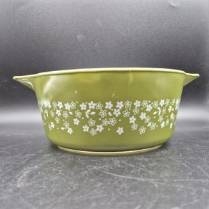 May include: A vintage green Pyrex bowl with white floral pattern. The bowl has a rounded shape with two handles and a white floral design around the middle. The bowl is likely made of glass.