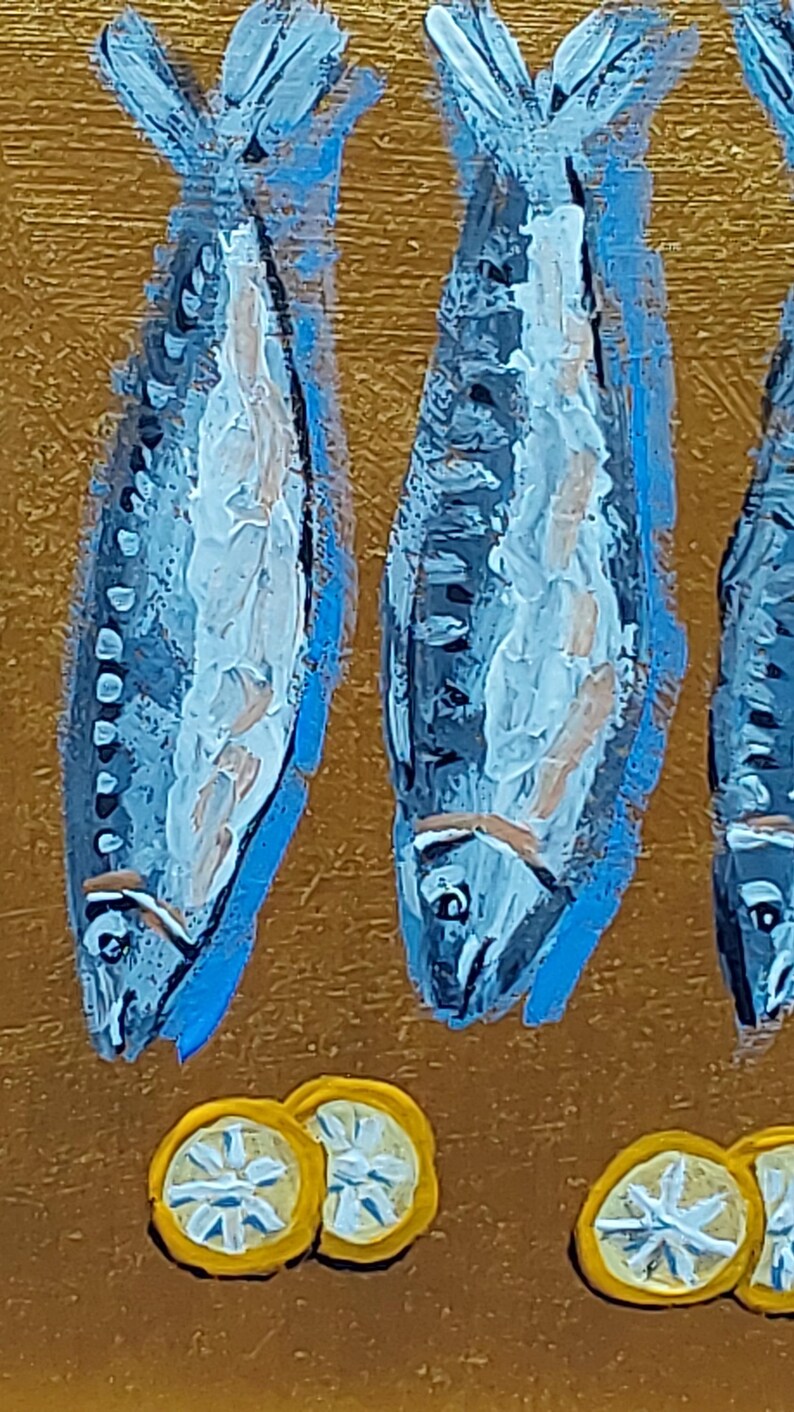 以下が含まれることがあります： 金色の背景に、青い魚が3匹描かれた芸術的な絵画。白とベージュのディテールが施されています。下部には黄色のレモンスライスがあります。この作品は、テクスチャのある塗装された外観をしています。