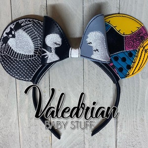 May include: Black and white mouse ears with a Jack Skellington and Sally design. The ears are made of felt and have a black headband. The headband has the text "Valedrian Baby Stuff" on it.