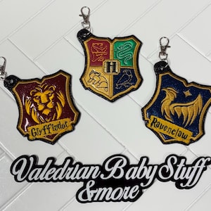 May include: Three embroidered keychains featuring the crests of Gryffindor, Hufflepuff, and Ravenclaw from the Harry Potter series. Each keychain has a metal clasp and is in the shape of a shield. The text "Valerian Baby Stuff & more" is also visible.