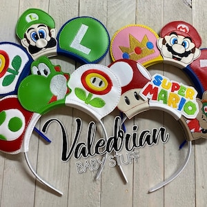 Op de afbeelding: Een verzameling Super Mario-thema haarbanden met verschillende personages en elementen uit het spel. Ontwerpen omvatten Mario, Luigi, Princess Peach, Yoshi en power-ups. De haarbanden zijn wit met kleurrijke karakterdetails.