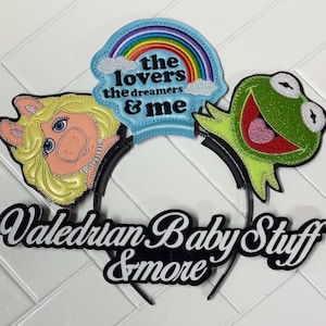 May include: A black headband featuring Miss Piggy, Kermit the Frog, and a rainbow design with the text "the lovers the dreamers & me." The headband also includes the text "Valedrian Baby Stuff & more."