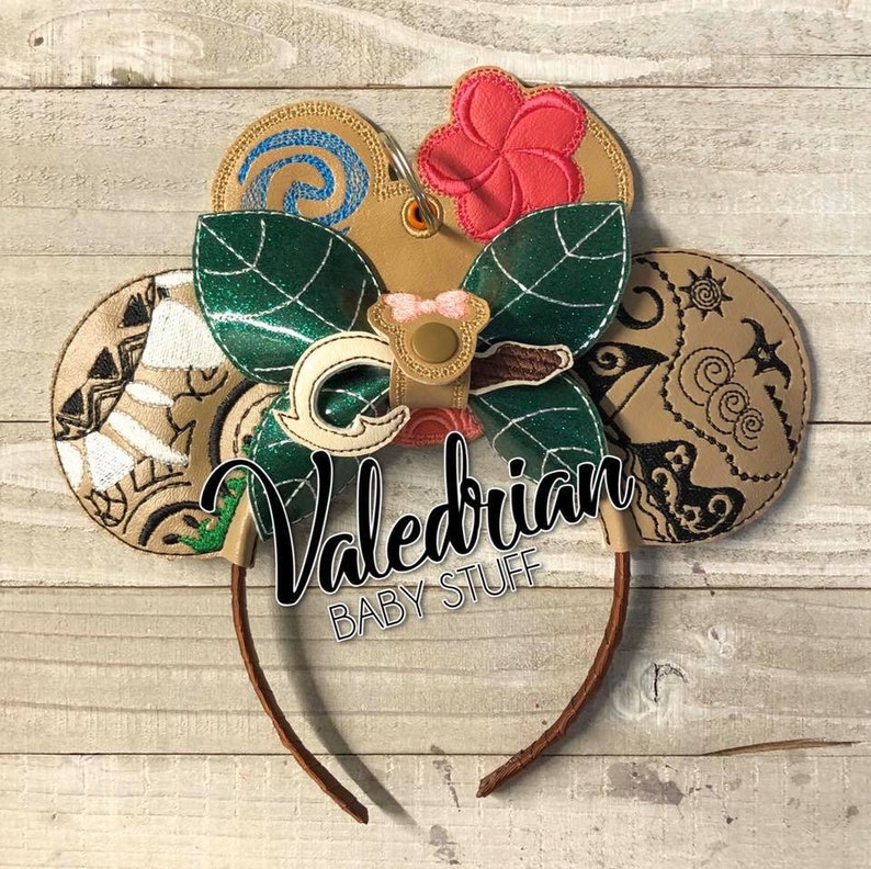 Puede incluir: Una diadema marr&oacute;n con elementos decorativos. Incluye orejas de Mickey Mouse de color beige con patrones bordados, un lazo verde en forma de hoja y una flor rosa. El texto "Valedrian BABY STUFF" es visible.
