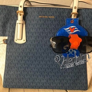 Puede incluir: Un bolso tote azul y blanco con un soporte para gafas de sol y gafas de sol. El bolso tiene un patr&oacute;n repetitivo y las palabras "MICHAEL KORS" son visibles. El soporte para gafas de sol es azul con un dise&ntilde;o de Mickey Mouse y el texto "Valedrian BABY STUFF".