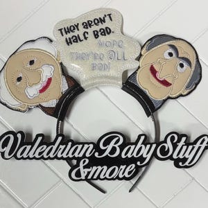 May include: A black headband featuring two cartoon character faces with embroidered details. A speech bubble with the text "THEY AREN'T HALF BAD. NOPE, THEY'RE ALL BAD!" is centered above the characters. The text "Valedrian Baby Stuff & more" is below.