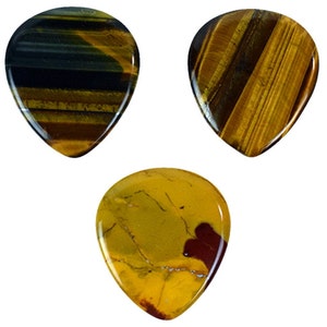 Puede incluir: Tres púas de guitarra hechas de ojo de tigre y piedra jaspe. Las púas tienen forma de lágrima y un acabado natural y pulido.