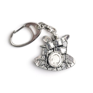 May include: A silver-toned metal keychain featuring a detailed miniature drum set. The keychain has a silver ring for attaching to keys.