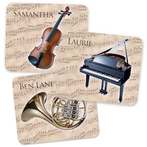 May include: Three personalised music note coasters featuring a violin, a grand piano, and a French horn. The coasters are beige with brown musical notes and the names "Samantha", "Laurie", and "Ben Lane" printed on them.