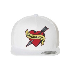 May include: White baseball cap with a red heart and arrow embroidered on the front. The heart has a yellow banner that reads "Rock & Roll".
