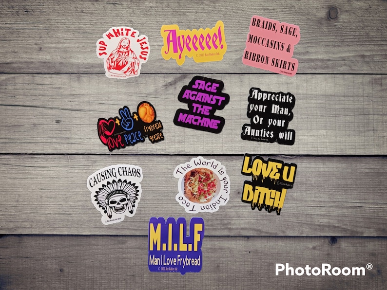 May include: A collection of colorful stickers with various phrases and designs. Some of the stickers feature religious imagery, while others have humorous or satirical messages. The stickers are arranged on a wooden surface.