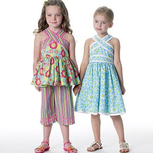 May include: Two young girls wearing matching floral and striped outfits. One girl wears a blue floral top and striped pants. The other girl wears a blue floral dress. Both outfits have criss-cross halter necklines and are paired with sandals.