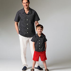 May include: A man and a child are wearing matching black button-down shirts with a white geometric pattern. The man wears white pants and the child wears red shorts. Both are wearing sandals. The background is a solid light gray.