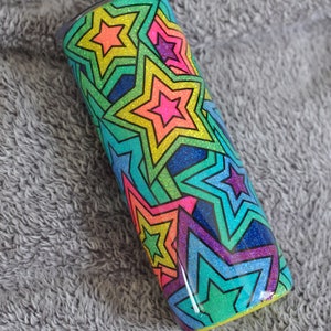 May include: A stainless steel tumbler with a colorful, glittery design of overlapping stars. The stars are outlined in black and filled with a rainbow of colors, including pink, blue, green, yellow, and orange.