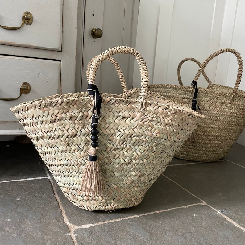 May include: Two large woven straw tote bags with black and white tassel accents. The bags have a natural, rustic look and are perfect for carrying groceries or other items.