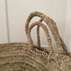 May include: A large, woven basket with two sturdy handles. The basket is made of natural, light brown straw and has a herringbone pattern.