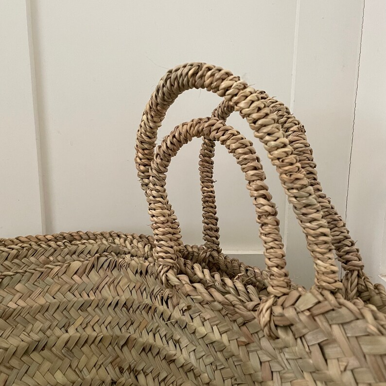 May include: A large, woven basket with two sturdy handles. The basket is made of natural, light brown straw and has a herringbone pattern.