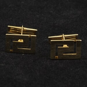 May include: A pair of gold cufflinks with a geometric design. The cufflinks are square shaped and have a Greek key pattern.