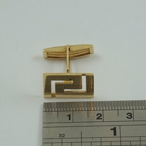 May include: Gold cufflinks with a Greek key design. The cufflinks are approximately 1 inch in length.