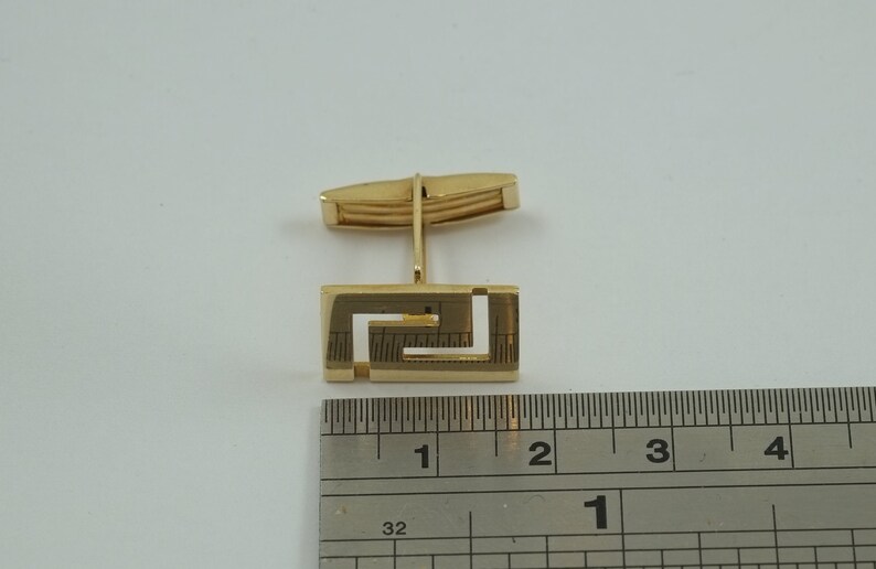 May include: Gold cufflinks with a Greek key design. The cufflinks are approximately 1 inch in length.