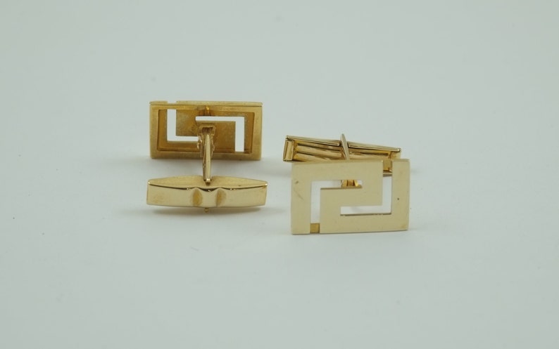 May include: A pair of gold cufflinks with a geometric design. The cufflinks are made of a shiny metal and have a square shape.
