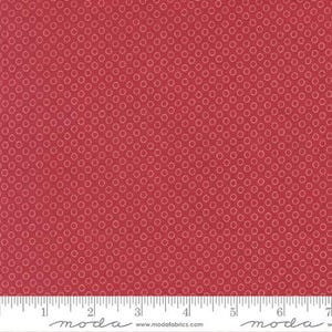 May include: Red fabric with a repeating pattern of small, light-colored circles. The fabric has a textured appearance and a ruler is visible at the bottom, indicating measurements in inches.