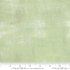 May include: A light green fabric with a textured, distressed appearance. The fabric has a subtle, mottled effect with lighter areas, creating a vintage or rustic aesthetic. The fabric is suitable for quilting and other craft projects.